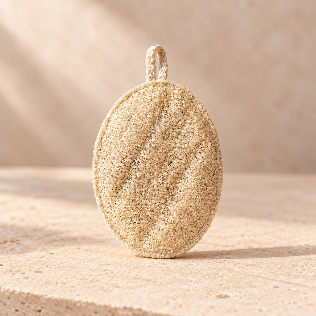 Estropajo ovalado de luffa natural de maro naturals con lazo de algodón sobre piedra beige.