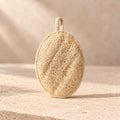 Estropajo ovalado de luffa natural de maro naturals con lazo de algodón sobre piedra beige.