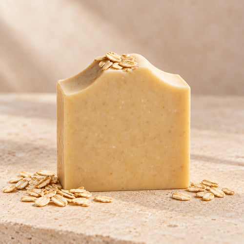 Jabón de avena de maro naturals, barra beige con hojuelas de avena sobre piedra clara.