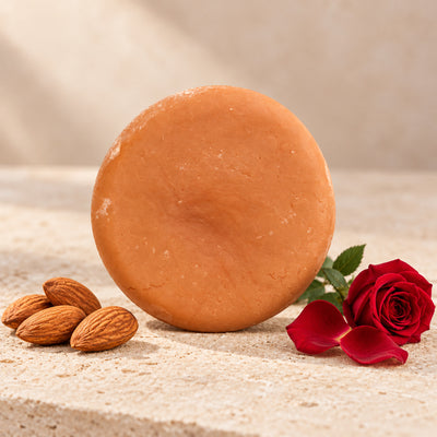 Shampoo sólido de rosas y almendras de maro naturals, barra color terracota junto a almendras y una rosa roja.